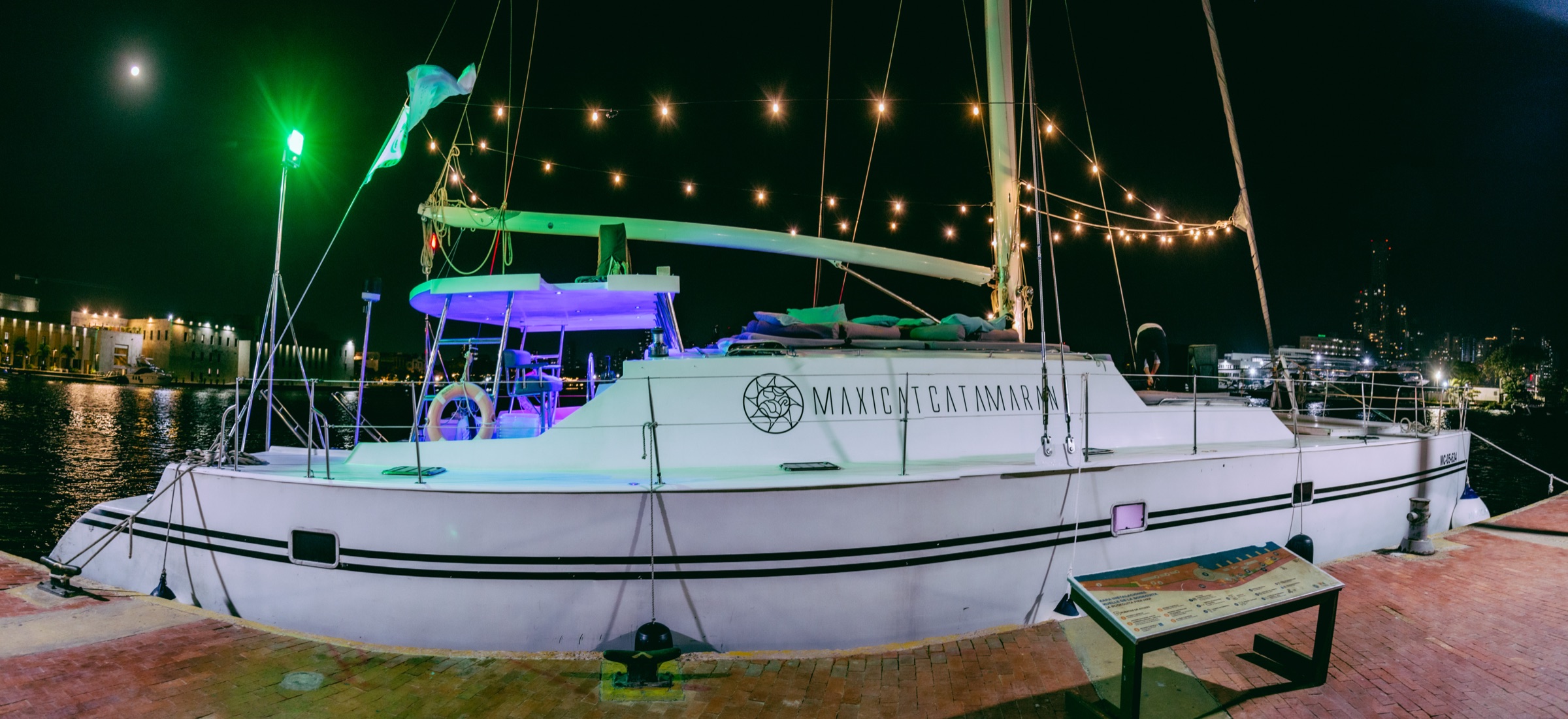 Catamarán Maxicat iluminado de noche en el muelle de Cartagena, listo para la fiesta de fin de año de una empresa